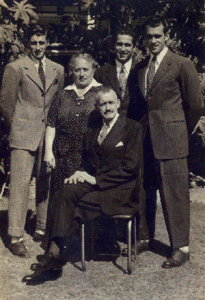 Father is seated; mother and three sons, stand. Men are dressed in business suits with ties.