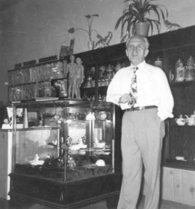 Mr. Greis leans on store case filled with items; shelves behind him hold other goods