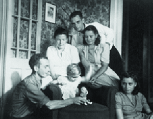 a family grouped around a chair, with a small child and her doll, in the center