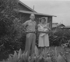 the couple stands in front of their bungalow; she holds a cat