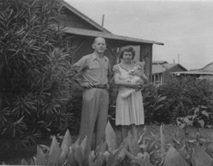 the couple stands in front of their bungalow; she holds a cat
