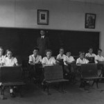 children at desks with teacher in the back