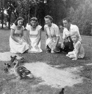 family group kneel on grass to watch duck and ducklings