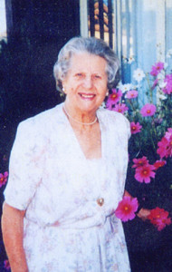 Gertrude Schneider smiling, in a floral dress; flowers in the background