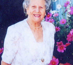 Gertrude Schneider smiling, in a floral dress; flowers in the background