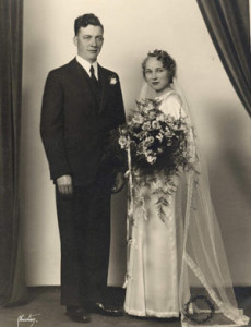 wedding portrait; groom in dark suit, bride in white satin with large bouquet