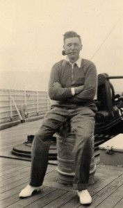 Karl Vogt sits on object on boat deck, smoking pipe