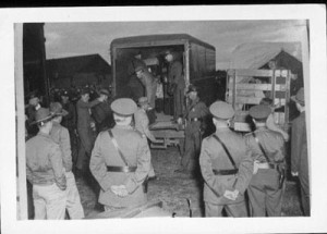 internees climbing out of truck back, watched by camp guards
