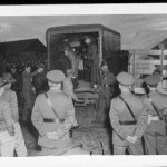 internees arriving by truck, with guards lined up in foreground