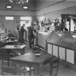 row of tables and a counter to the right; men seated and standing at the counter, with food
