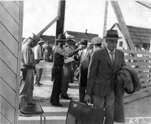 men with suitcases, lined up in front of soldiers, prior to departure