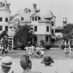 3 story building with turrets in background, with dancing circles of women and audience in foreground