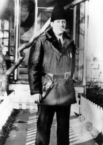 man in warm jacket and hat, with gun in holster and smoking cigarette
