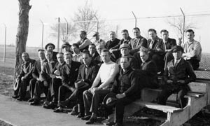 group of internees on small bleachers, with barbed wire fence behind them