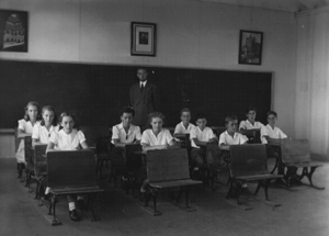children at school desks, with teacher in the background